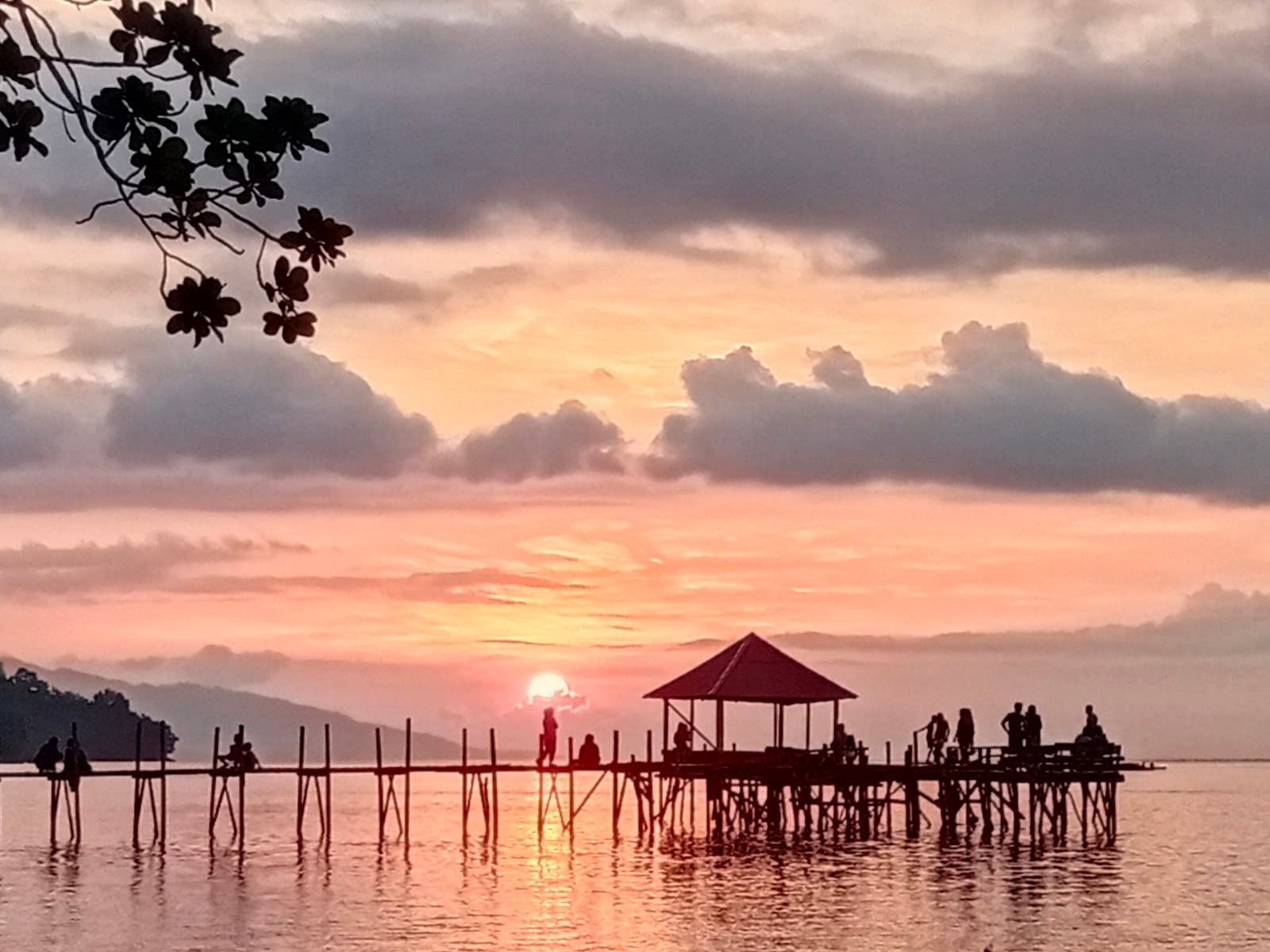 Matahari terbenam jingga di balik dermaga dan gazebo Pantai Memit, Shafira Resort Morella